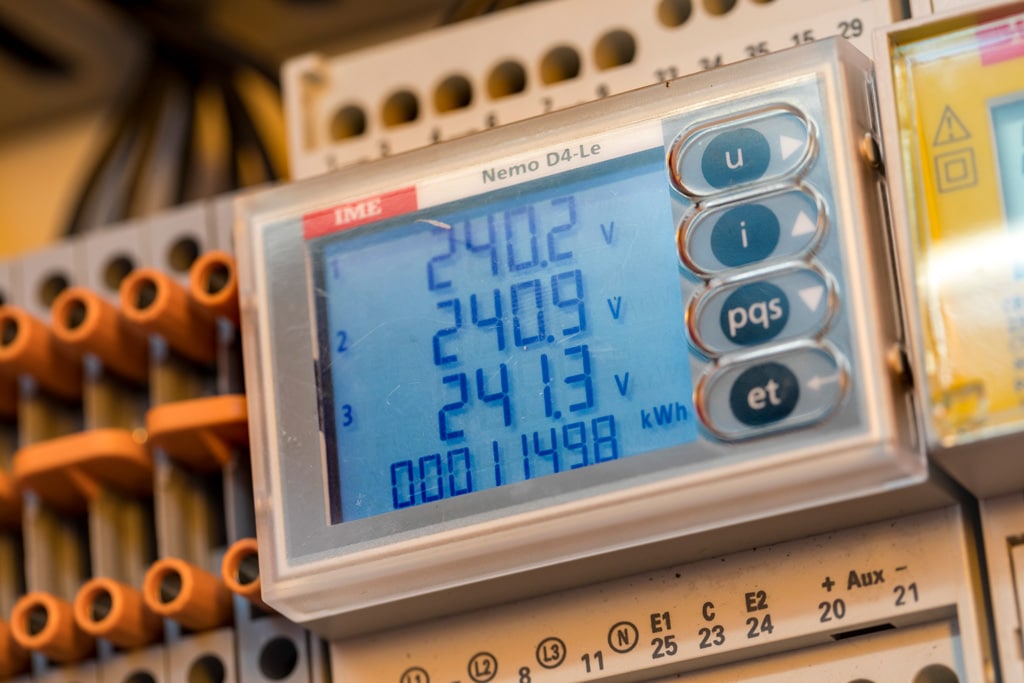 Close-up of a digital electrical power meter displaying voltage readings inside a switchboard.